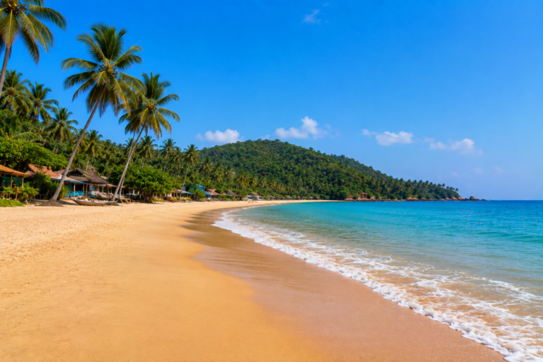 Scenic palm-lined Vagator Beach in North Goa with golden sand, turquoise Arabian Sea and green headland